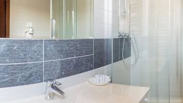 Een moderne badkamer met een grote spiegel, een douchecabine en een wastafel met toiletartikelen.