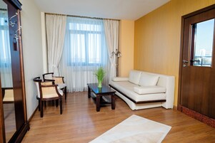 Una sala de estar con sofá, sillas, una mesa de centro y un amplio ventanal con cortinas.