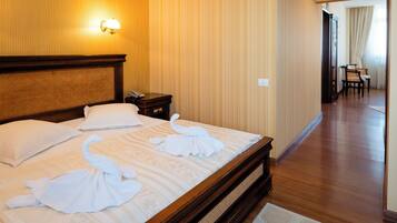 A hotel room with a wooden headboard, a bed with white linens and towels, a nightstand, and a wall-mounted lamp.