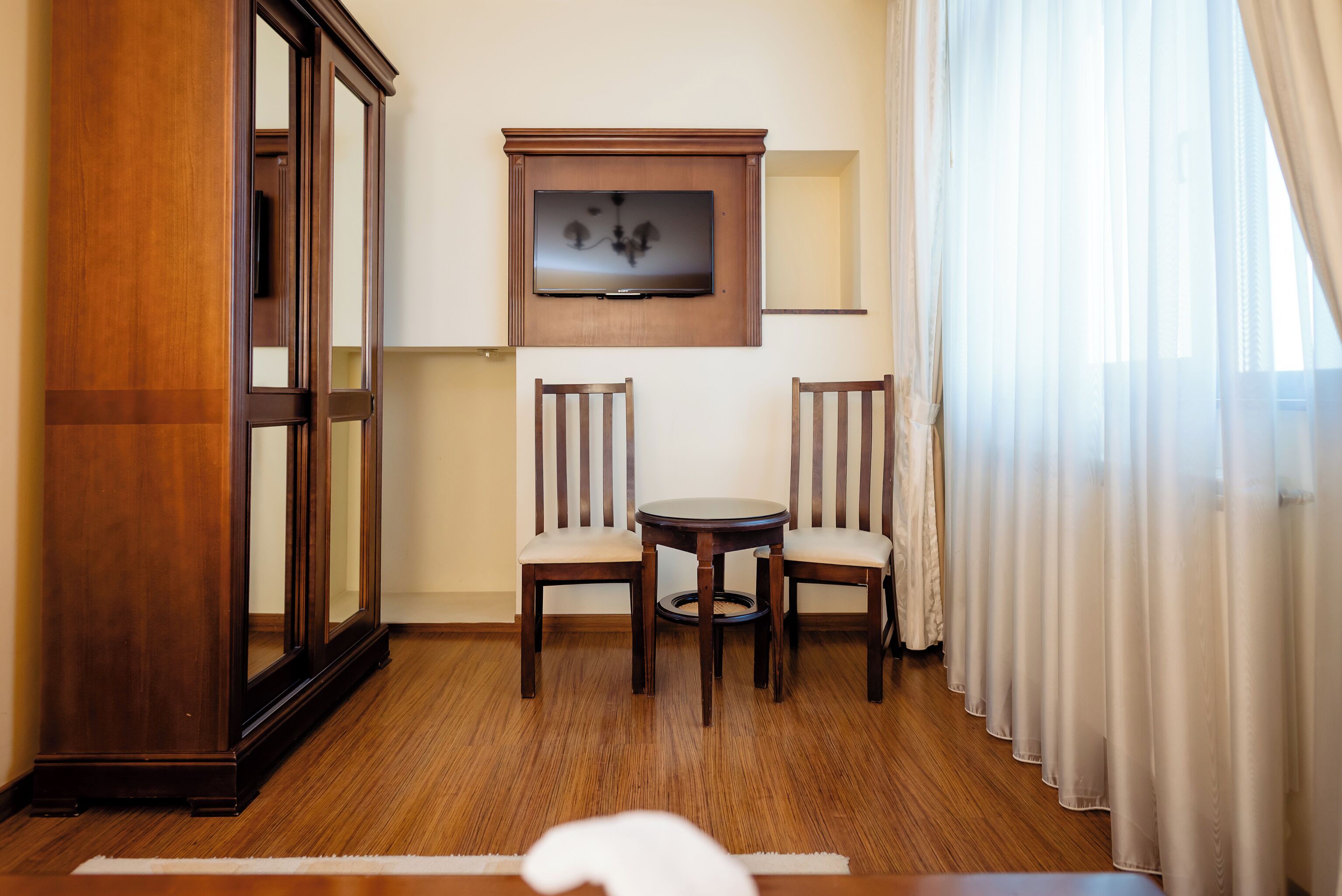 Une chambre d’hôtel avec un plancher en bois, un téléviseur fixé au mur, deux chaises en bois et une petite table ronde.