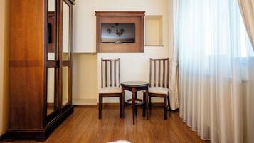 Une chambre d’hôtel avec un plancher en bois, un téléviseur fixé au mur, deux chaises en bois et une petite table ronde.