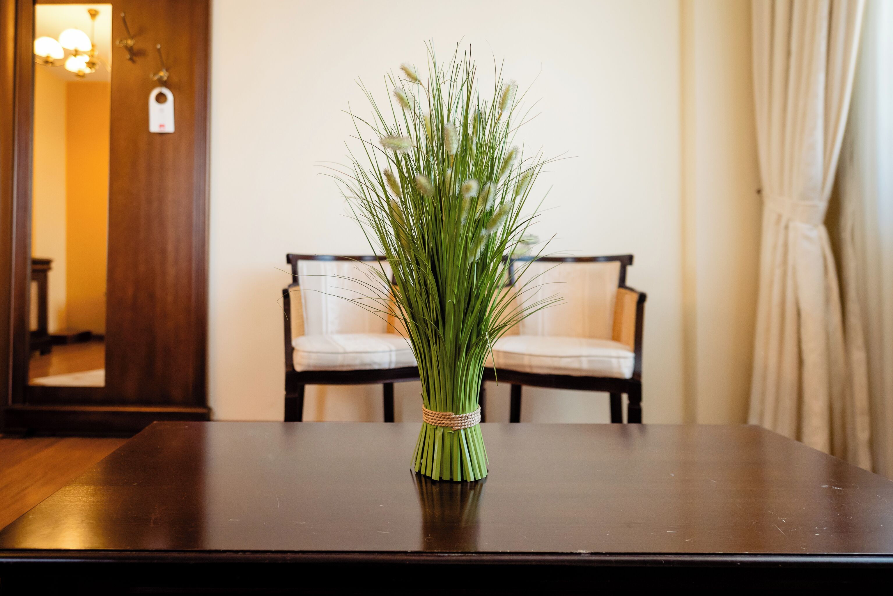 Una mesa de madera con un jarrón de pasto verde en el centro.