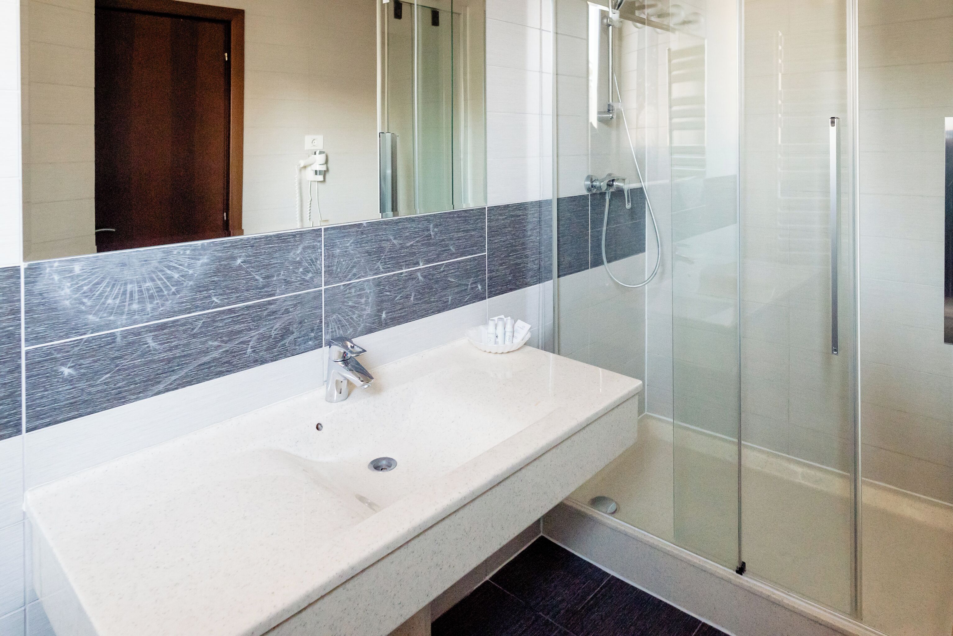 Un baño moderno con un lavamanos blanco, cabina de ducha de vidrio y un salpicadero de azulejos oscuros.