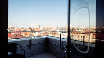 A balcony with a view of a cityscape, a chair, and a glass door with a logo.