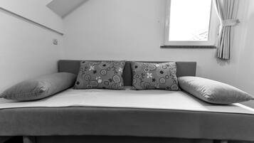 Un dormitorio minimalista con cama, dos almohadas estampadas, una ventana con cortinas y techo inclinado.