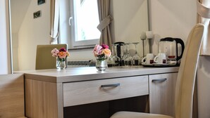 Habitación de hotel con un escritorio de madera, dos jarrones con flores, una cafetera y un espejo que refleja la habitación.