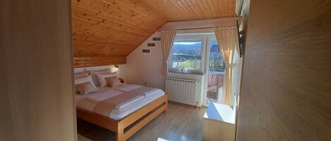 Un dormitorio con techo de madera, una cama con ropa de cama blanca, una ventana con cortinas y vistas al exterior.