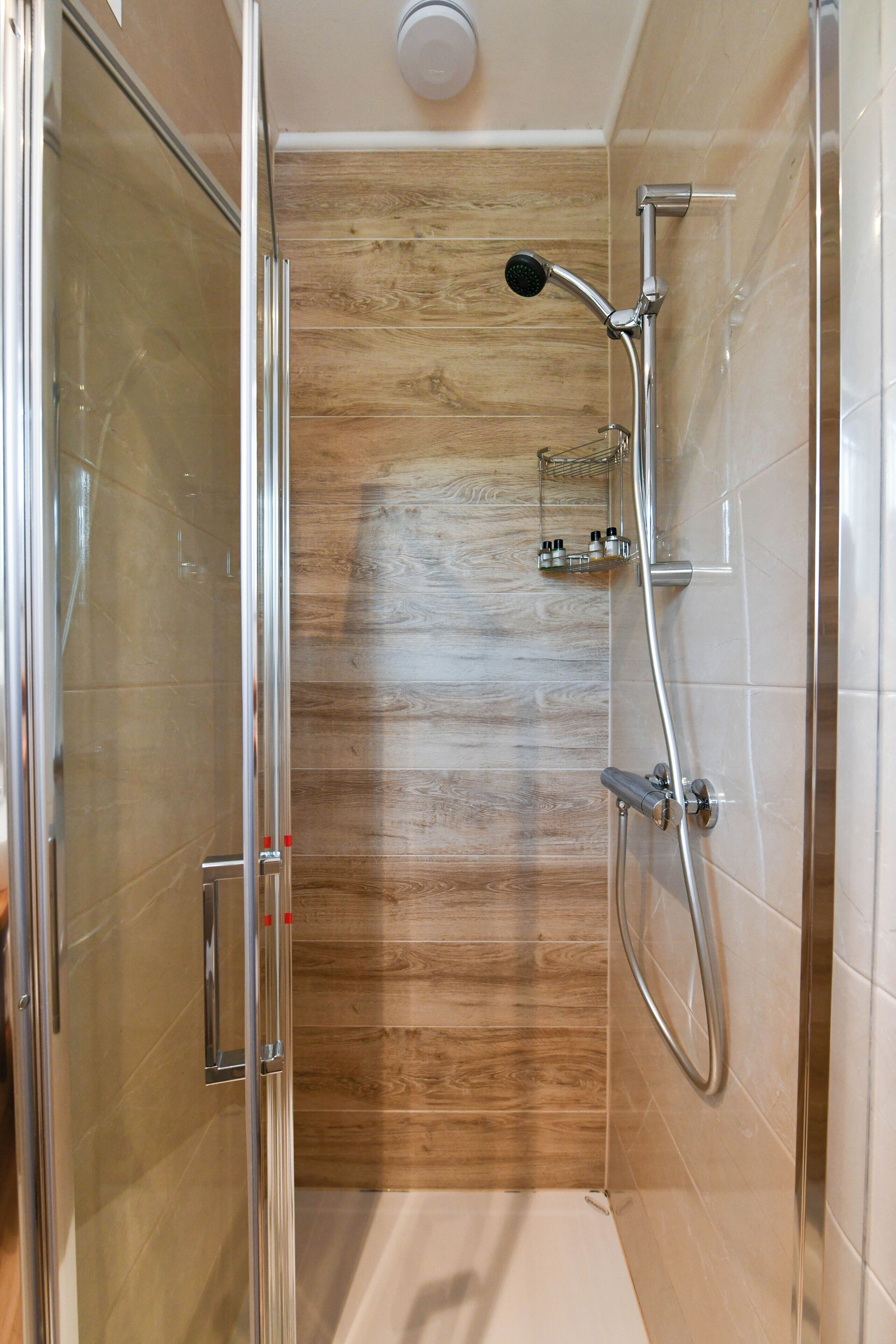 A glass-enclosed shower with a wooden panel wall, a handheld showerhead, and a wall-mounted faucet.