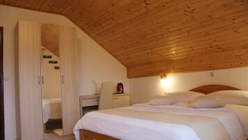 A bedroom with a wooden ceiling, a bed with white bedding, a nightstand with a red kettle, and a wardrobe with a mirror.