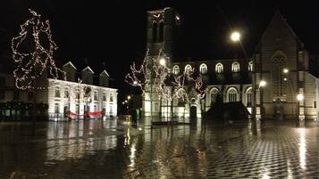 A historic square with a church, a bell tower, and illuminated trees.
