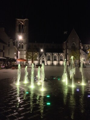 A nighttime view of a square with a fountain, a church, and a tower.