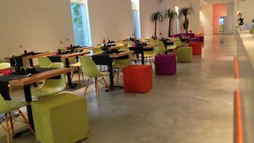 Un salón de conferencias moderno con filas de mesas y sillas, ventanas amplias y plantas en macetas.