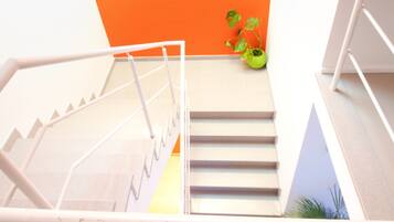 A staircase with white railings, a green plant, and a bright orange wall.