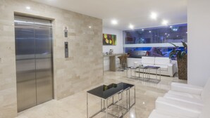 A modern lobby with a reception desk, a white sofa, a glass coffee table, and an elevator. - Basic Hotel Centenario by Hoteles MS (Cali)