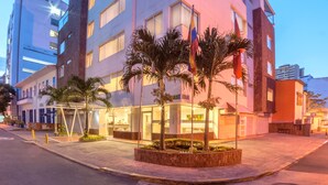 A multi-story hotel with a modern design, featuring a central courtyard with palm trees and a flagpole. - Basic Hotel Centenario by Hoteles MS (Cali)