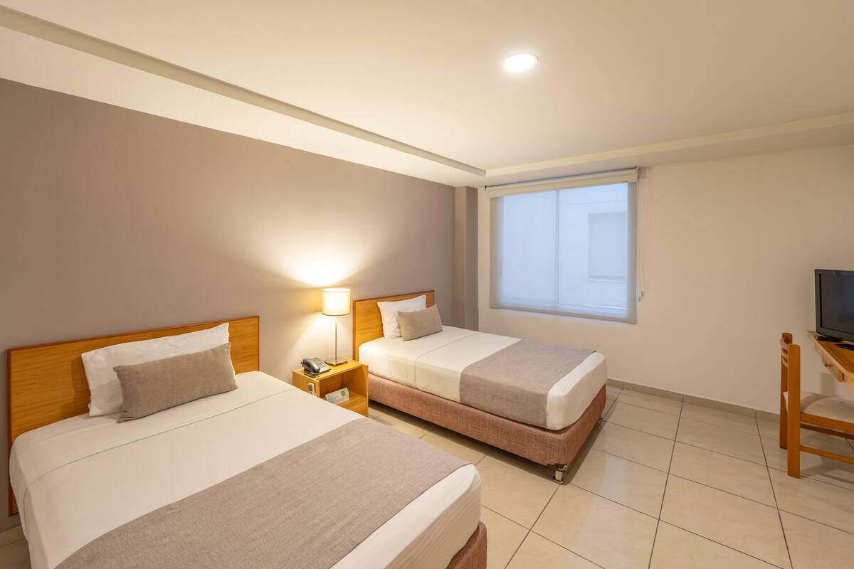 A hotel room with two beds, a TV, a desk, and a window.