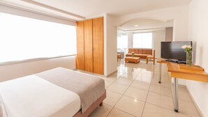 A modern hotel room with a large bed, a TV, a wooden wardrobe, a sofa, and a dining table. - Basic Hotel Centenario by Hoteles MS (Cali)