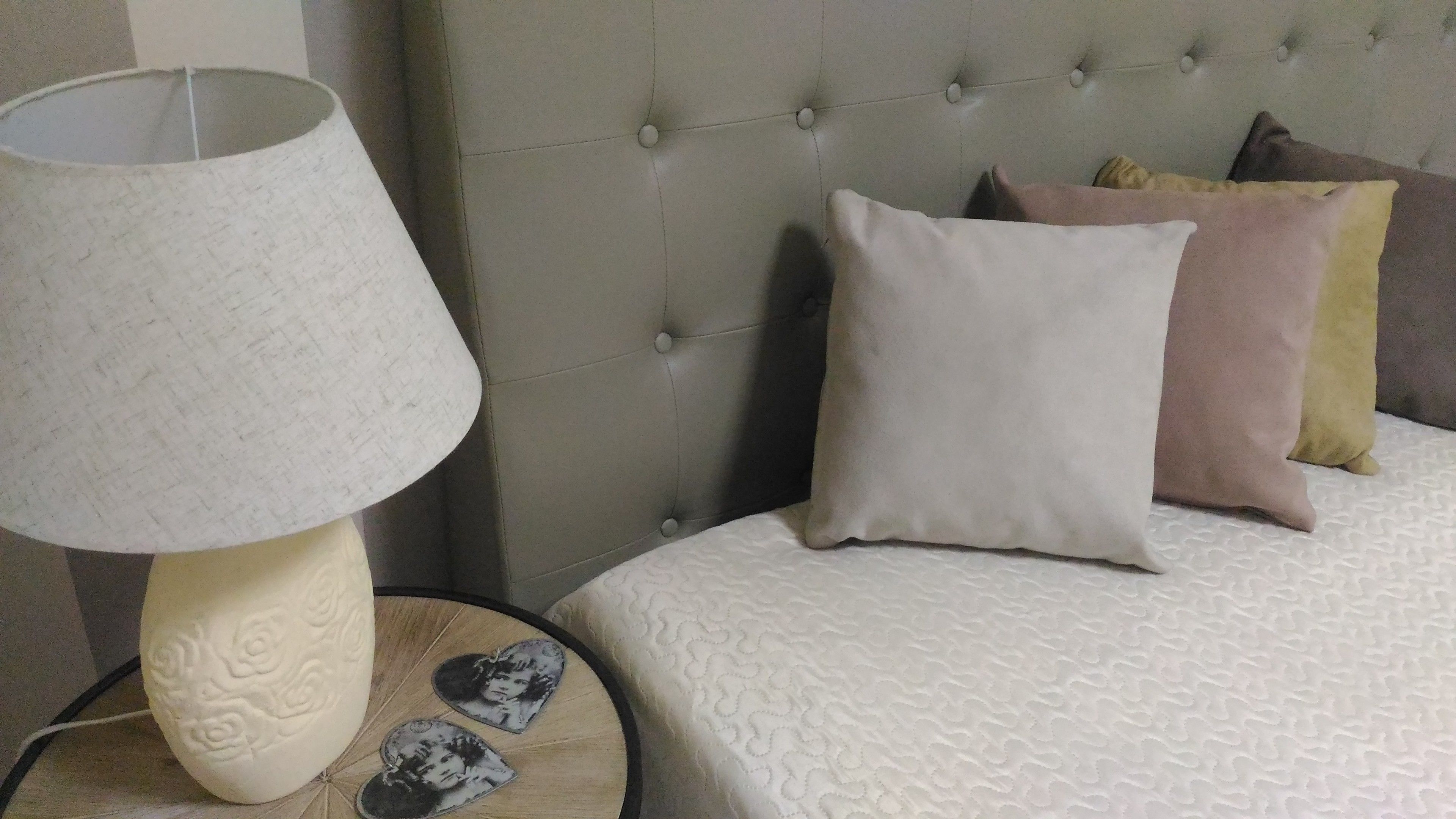 Ein Bett mit gestepptem Kopfteil, einer Nachttischlampe und mehreren Kissen.