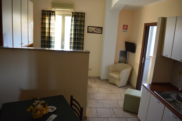 A compact kitchen with a dining area, a small sofa, and a flat-screen TV. - Hotel Residence Sirio (Reggio Calabria)
