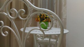 A white metal chair with a green vase of flowers on a small round table. - Hotel Residence Sirio (Reggio Calabria)