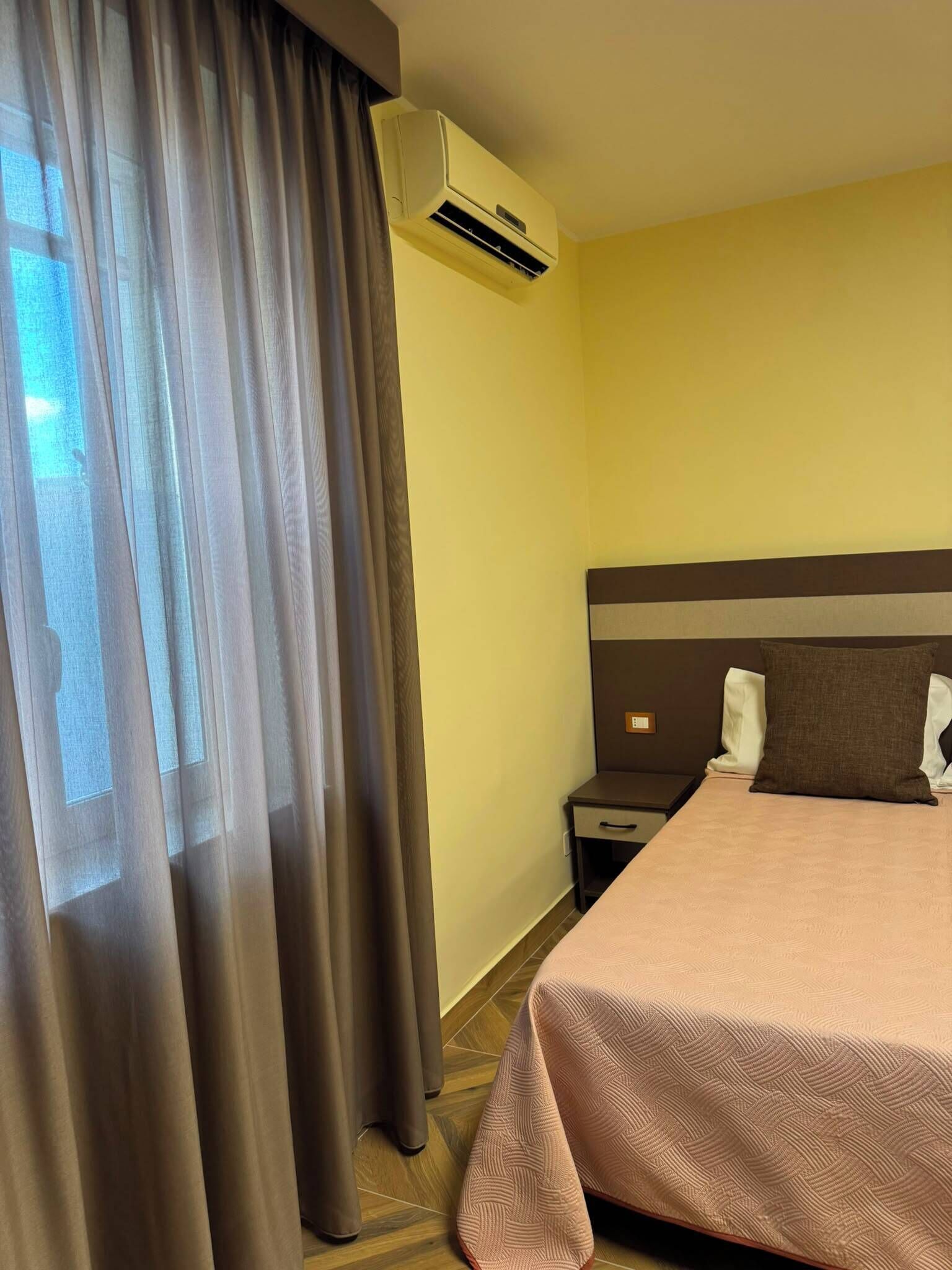 Une chambre d’hôtel équipée d’un lit, d’une table de chevet, d’un appareil de climatisation et d’une fenêtre avec des rideaux.