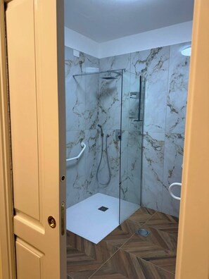 A modern bathroom with marble walls, a glass shower enclosure, and a herringbone-patterned floor. - Hotel Residence Sirio (Reggio Calabria)