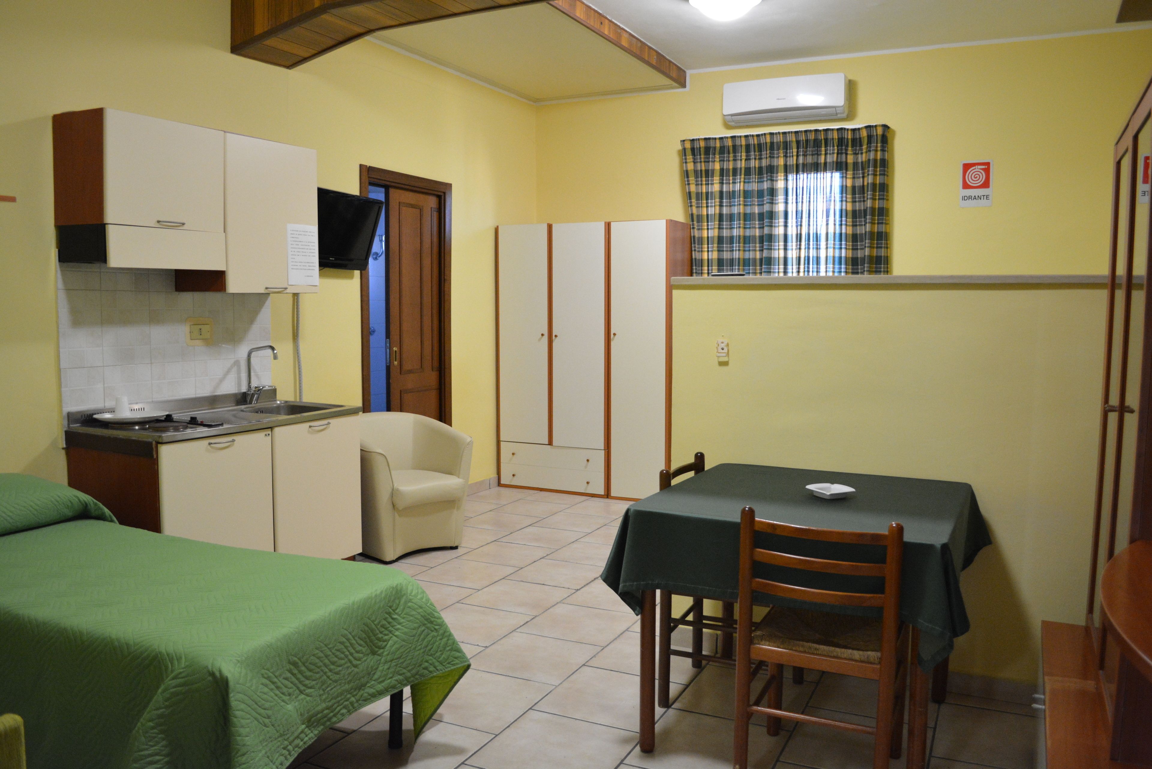 Una habitación compacta con kitchenette, una mesa de comedor con sillas, una cama individual y un armario.
