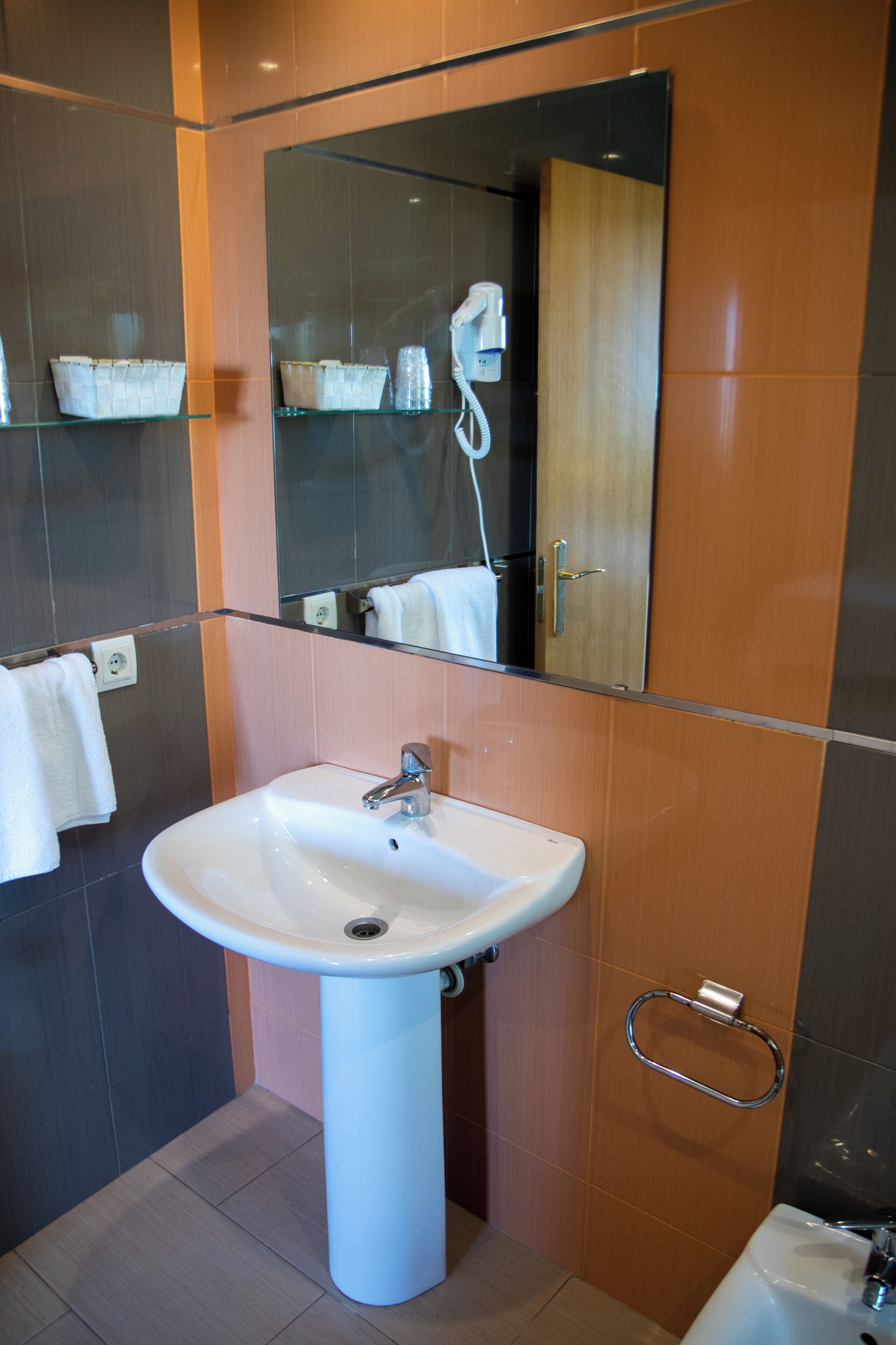 Un baño con un lavamanos blanco, un espejo y un perchero para toallas.