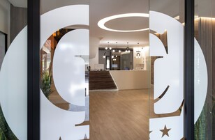 A reception area with a modern design, featuring a reception desk, a staircase, and a glass partition with a large 'G' logo.
