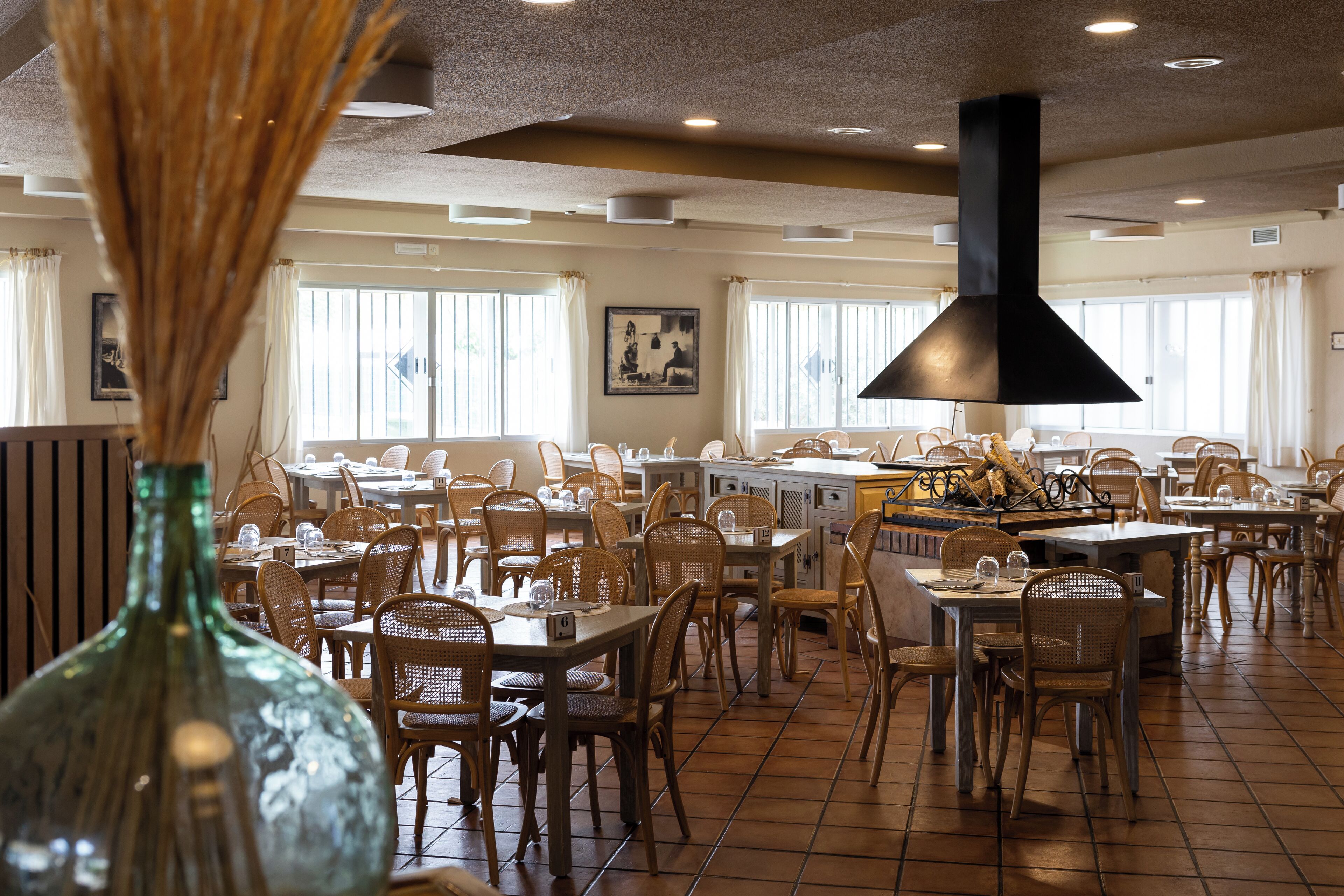 A spacious restaurant with multiple dining tables and chairs, large windows, and a prominent black chimney.