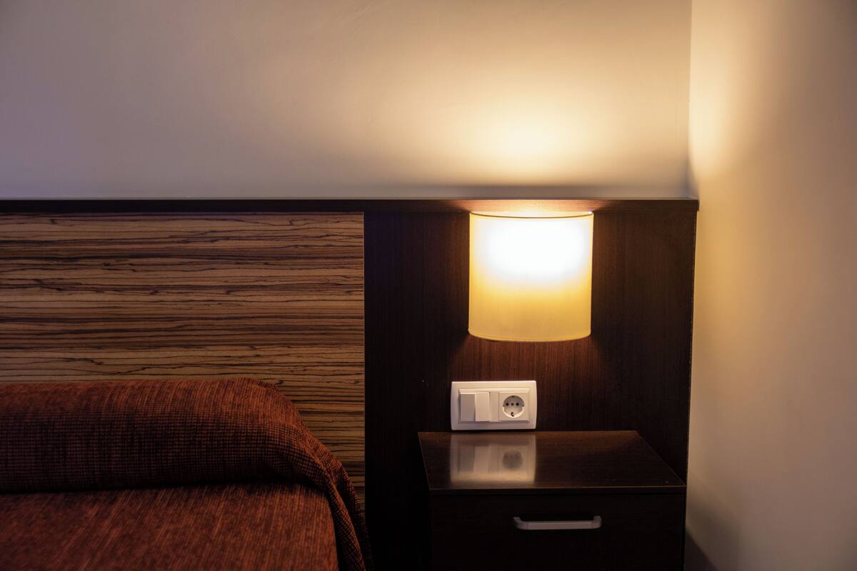 Habitación de hotel con panel de pared de madera, una mesita de noche con lámpara y un enchufe.