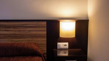 A hotel room with a wooden wall panel, a bedside table with a lamp, and a power outlet.