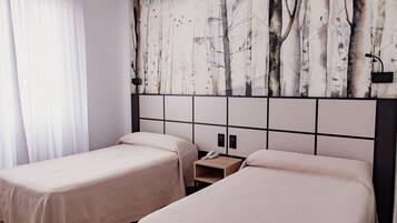 Habitación de hotel con dos camas, una mesita de noche y un mural de árboles en la pared.