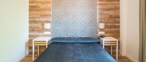 A single bed with a blue mattress, two bedside tables with lamps, and a patterned wall.