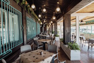 An outdoor dining area with tables and chairs, hanging pendant lights, and potted plants.