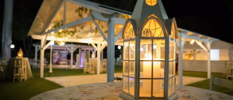 A lantern on a table with a floral tablecloth, a white gazebo in the background, and a grassy area.