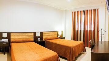 Habitación de hotel con dos camas, un escritorio, una silla, una lámpara y una cortina.