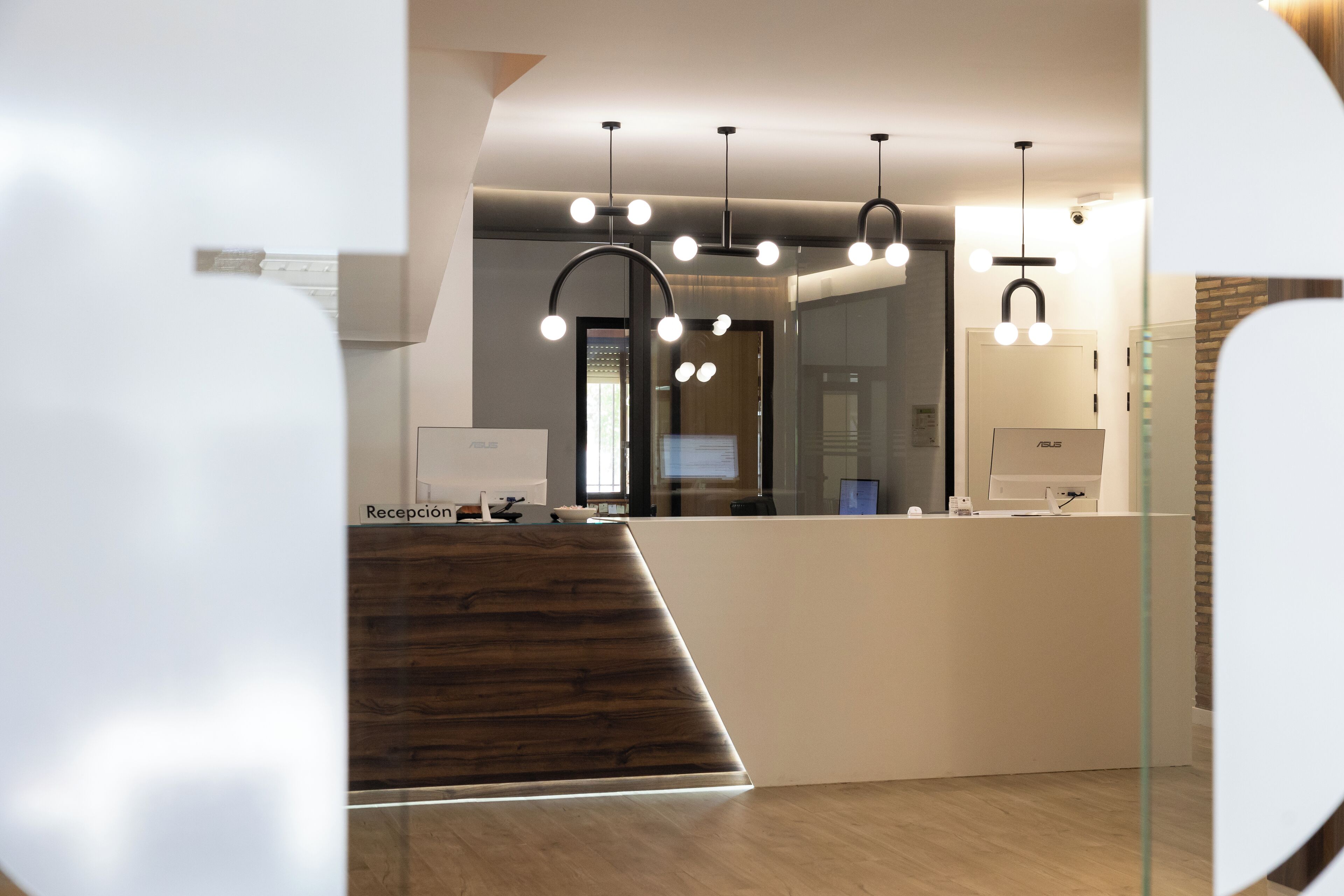 A modern reception area with a wooden reception desk, a glass partition, and a staircase leading to an upper level.