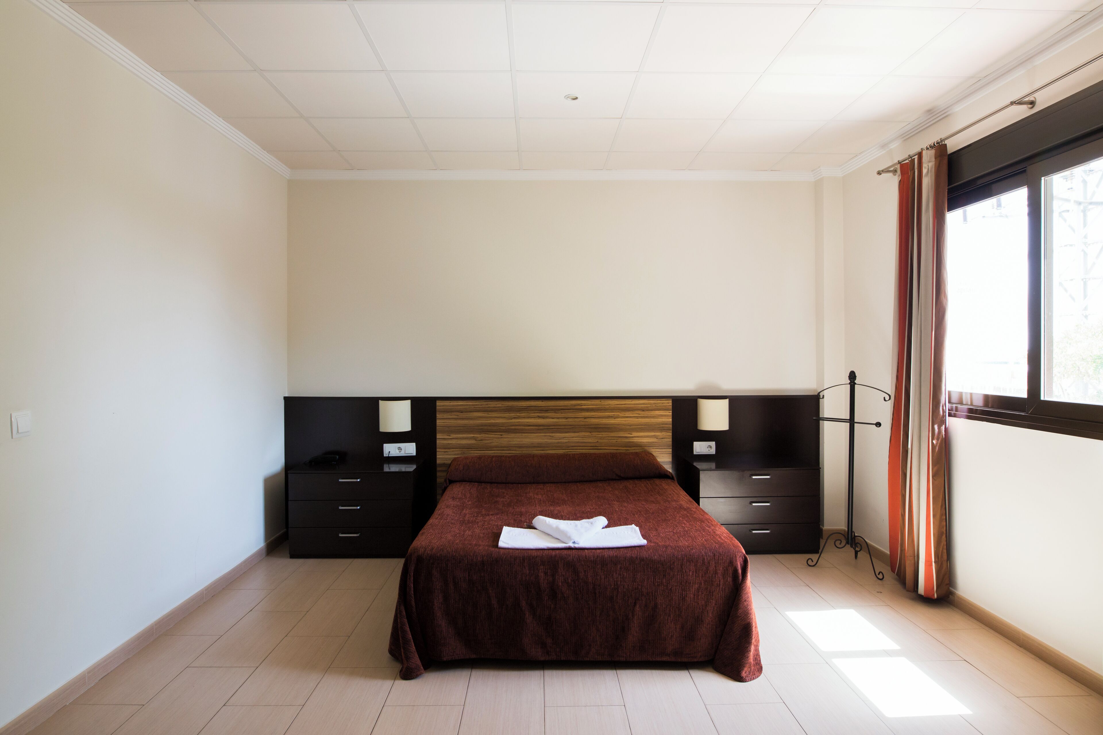 Une chambre à coucher avec un grand lit, une tête de lit en bois, deux tables de chevet et une fenêtre avec des rideaux.