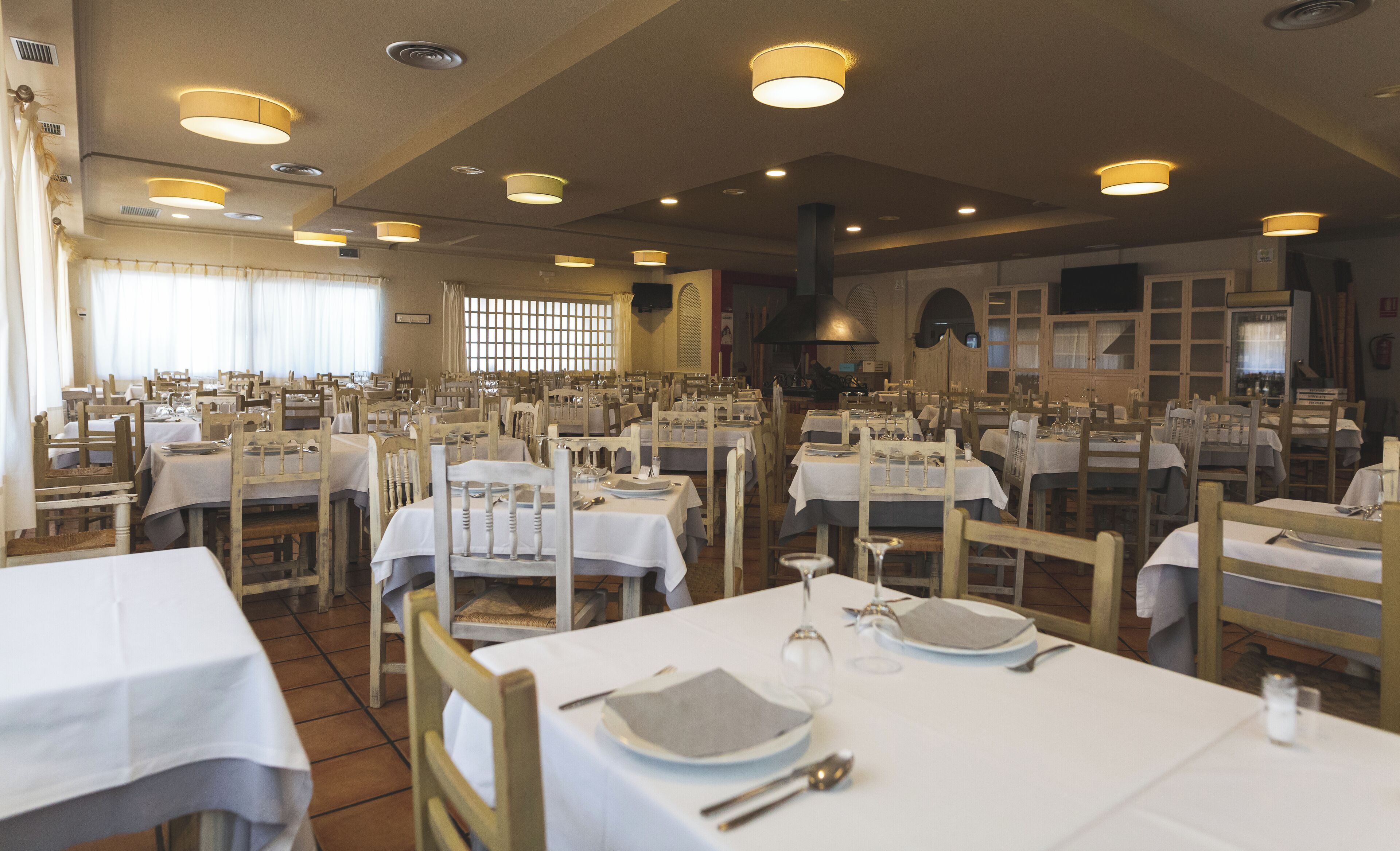 A restaurant with multiple tables set for dining, featuring wooden chairs and white tablecloths.