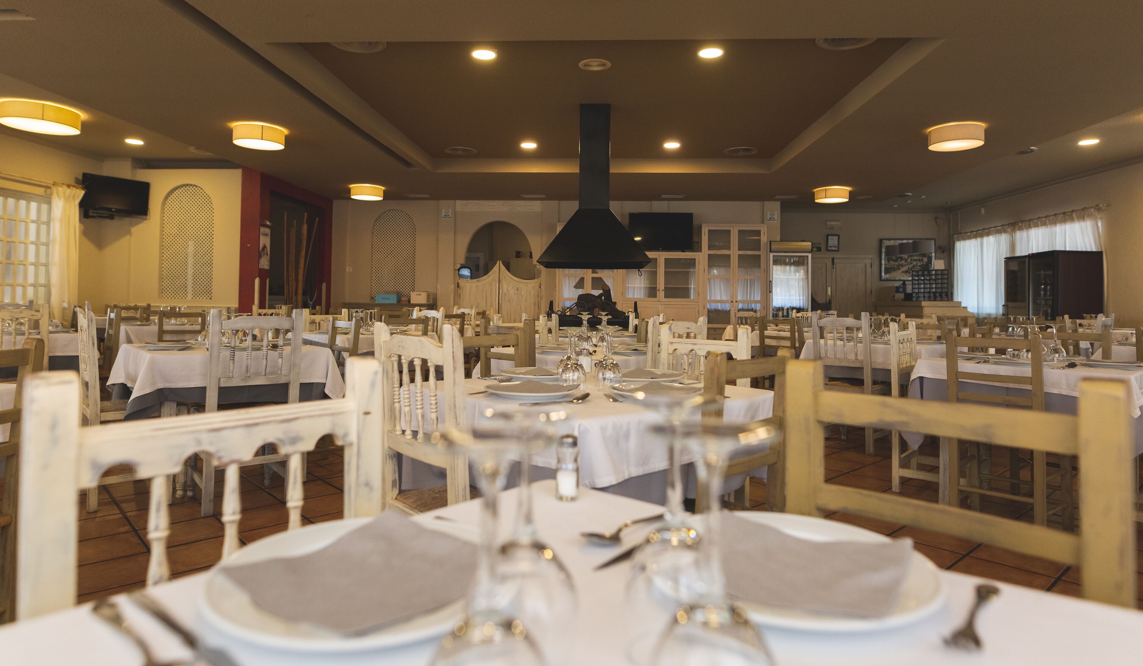 A restaurant with multiple tables set for dining, featuring white tablecloths and wooden chairs.