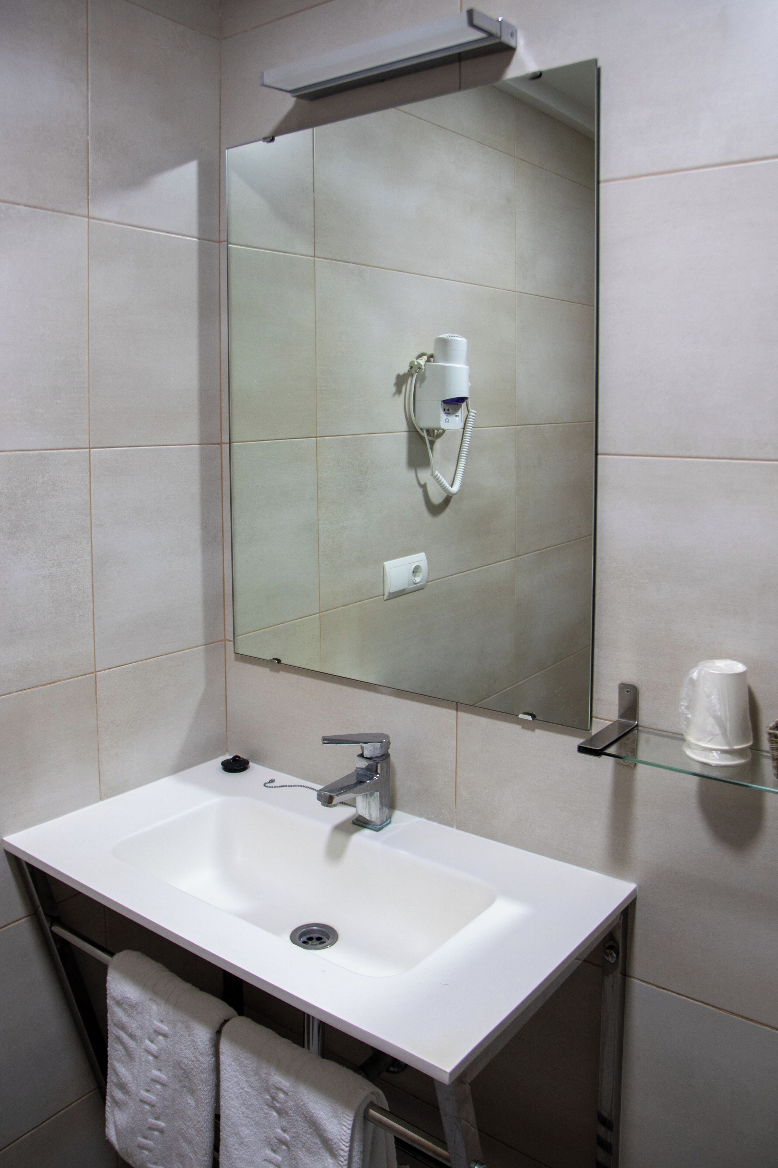 A bathroom with a white sink, a mirror, a hairdryer, and a glass shelf.