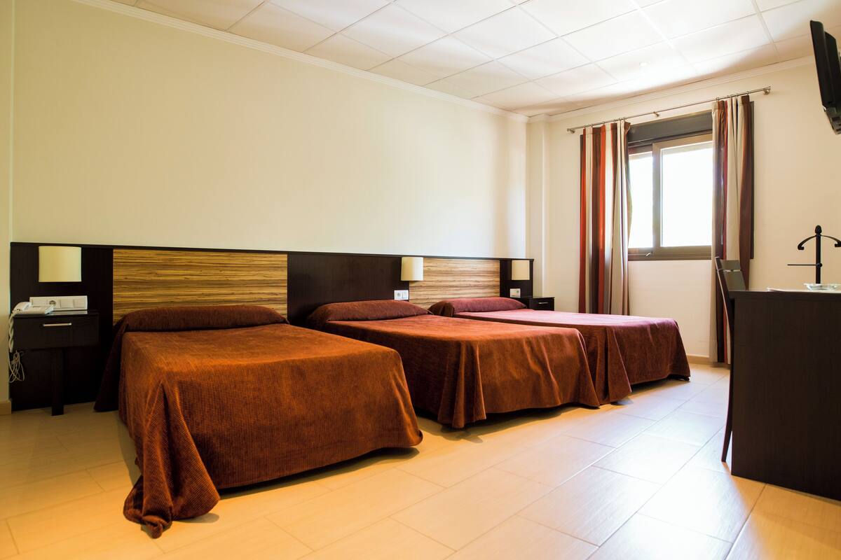 Habitación de hotel con dos camas, un escritorio y una ventana con cortinas.