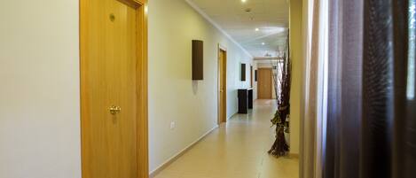 Un pasillo de hotel con puertas de madera, piso de baldosas e iluminación empotrada en el techo.