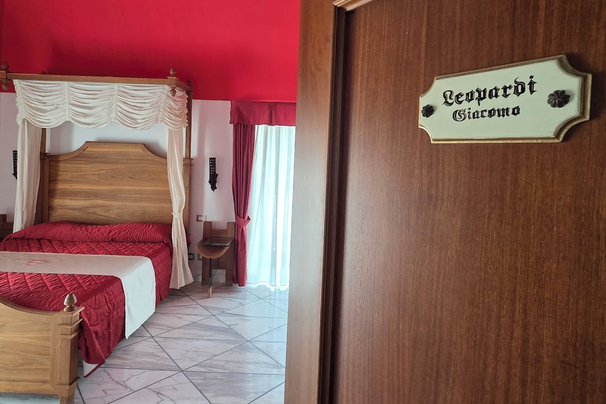 A bedroom with a wooden bed, a red ceiling, a wooden door with a nameplate, and a tiled floor.