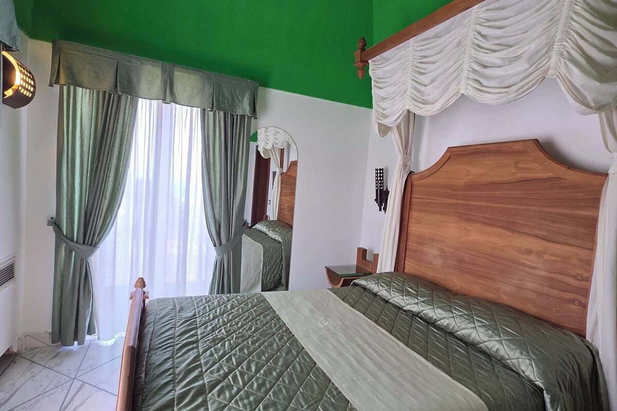 A room with a large bed, a wooden headboard, a green wall, and a window with curtains.