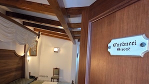 A bedroom with a bed, wooden beams, a sign reading 'Carducci Biosoque', a chair, and a small table. - Antico Casale Russo (Piano di Sorrento)