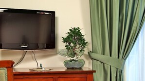 A room with a wooden dresser, a flat-screen TV mounted on the wall, and a potted plant on the dresser. - Antico Casale Russo (Piano di Sorrento)