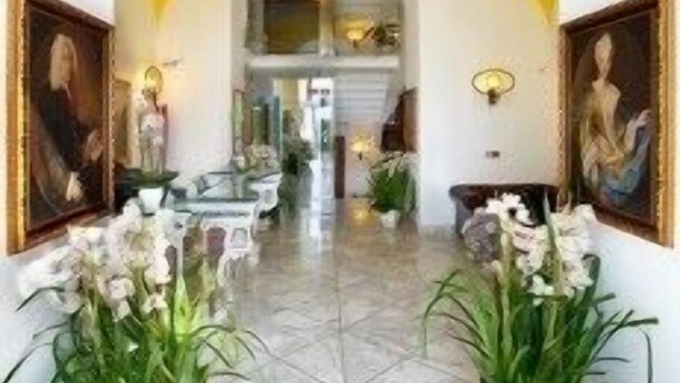 A hallway with a yellow archway, framed paintings, and potted plants. - Antico Casale Russo (Piano di Sorrento)