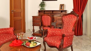 A room with a wooden desk, two red upholstered chairs, a round wooden table with fruit and glasses, and a red curtain. - Antico Casale Russo (Piano di Sorrento)